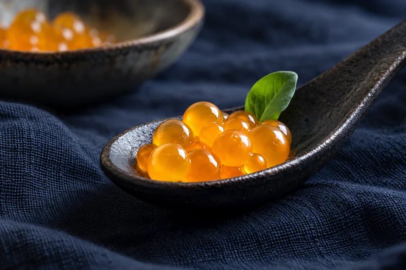 Kleine orangefarbene Sphären auf einem Keramiklöffel